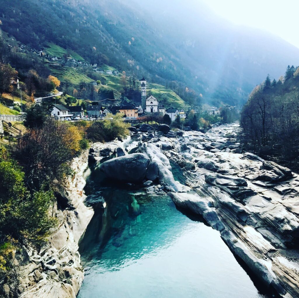 Turkusowa woda i skały w górskim potoku, w tle miasteczko z kościołem i zielone wzgórze w Ticino - Szwajcaria z dzieckiem