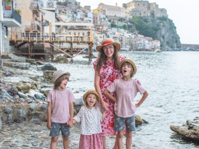 Mama w kolorowej sukience i kapeluszu stoi z dziećmi na tle morza i miasteczka na skale w Kalabrii we Włoszech - Kalabria z dziećmiria z dziećmi